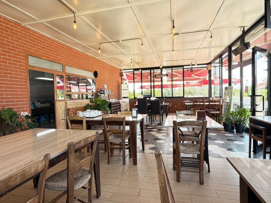 The Garden iç mekânı — ahşap masalar, sıcak aydınlatma ve bahçe manzaralı geniş pencereler
